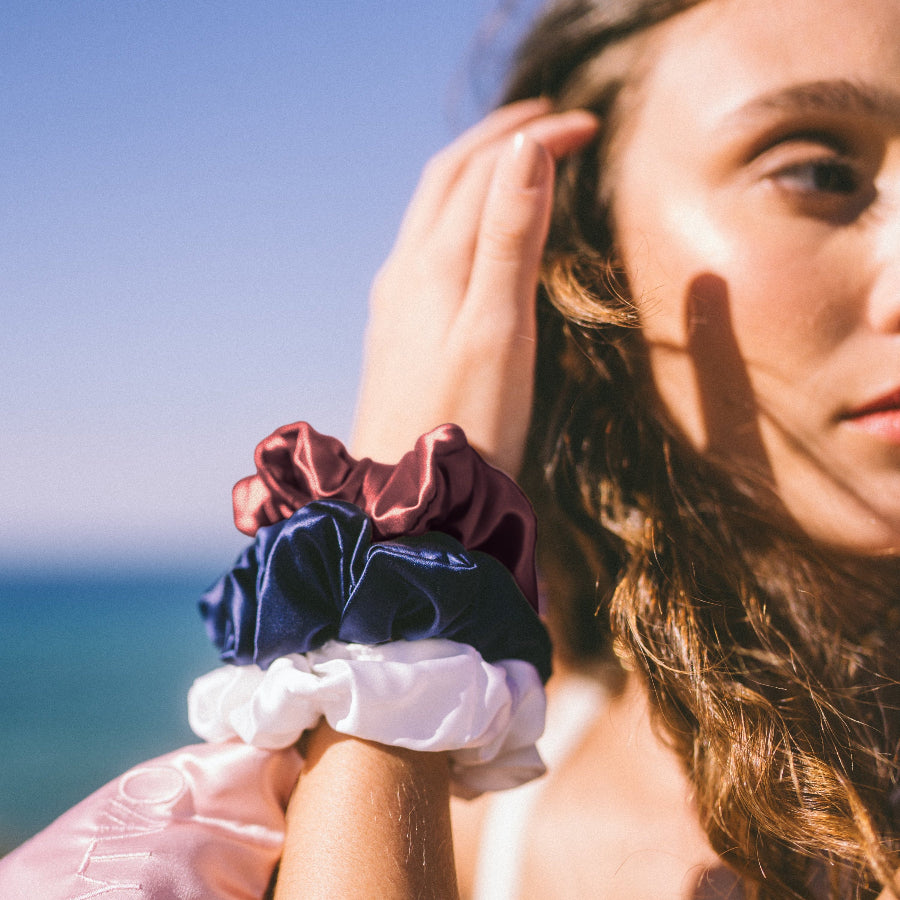Woman wearing colorful scrunchies on a beach with blue sky and ocean in the background