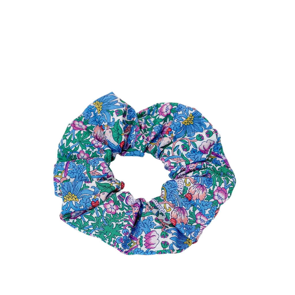 A fabric scrunchie with a dense floral print in blue, green, pink, and purple, photographed on a clean white background.