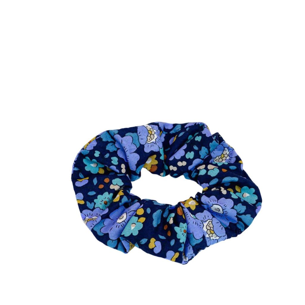 A fabric scrunchie with a dark navy blue background and a colorful floral pattern in shades of purple, blue, and yellow, photographed on a clean white background.